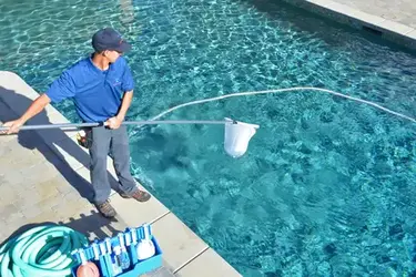 Un homme en chemise bleue et en short bleu assure le nettoyage d'une piscine à Agadir, dans le cadre d'un service de nettoyage professionnel.