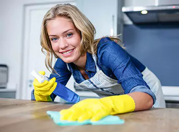 Une employée d'une société de nettoyage à Agadir porte un uniforme et des gants jaunes tout en tenant une éponge de nettoyage bleue.