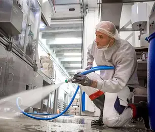 Un professionnel équipé de vêtements de protection effectuant un nettoyage à Agadir avec un équipement de pulvérisation, dans un environnement industriel ou de laboratoire, pour le compte d'une société de nettoyage.