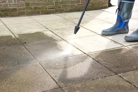 Une personne lave sous pression une terrasse pour enlever la saleté et la crasse, mettant en avant l'importance du nettoyage du sol pour maintenir un environnement propre.