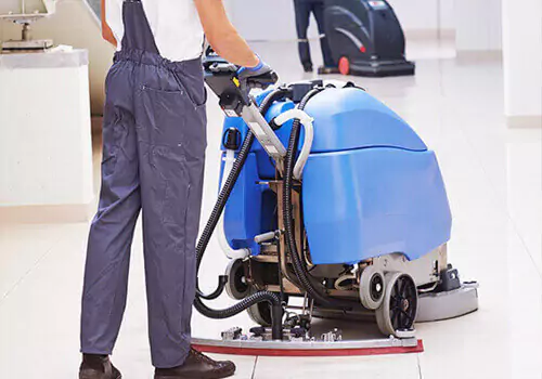 Un homme utilise une machine de nettoyage de sol bleue pour nettoyer le sol, illustrant le service de nettoyage des locaux commerciaux.