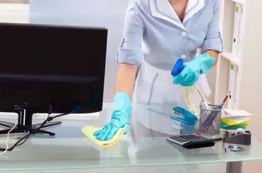 Une femme de ménage portant des gants bleus s'attelle à ranger un bureau à Agadir, dans le cadre d'un service de nettoyage professionnel.