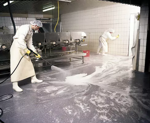 Deux ouvriers nettoient une pièce avec une substance blanche, assurant ainsi un environnement impeccable dans le cadre du nettoyage des usines.