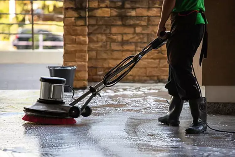 Personne utilisant une cireuse sur un sol en béton pour nettoyer et entretenir sa surface lisse, démontrant ainsi l'importance du nettoyage du sol.