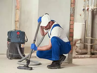 Un homme en salopette s'applique avec assiduité à nettoyer le sol avec un aspirateur, assurant ainsi un environnement impeccable et bien rangé lors du nettoyage de fin de chantier.