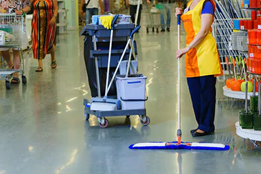 Une femme nettoie une allée de magasin, assurant la propreté et l’ordre, dans le cadre du service de nettoyage des locaux commerciaux.