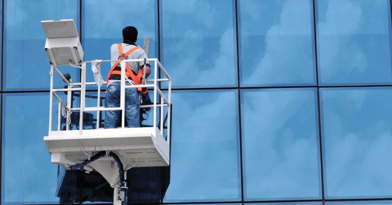 Travailleur en équipement de sécurité sur un ascenseur nettoyant les fenêtres d'un grand bâtiment, démontrant le service professionnel de nettoyage des vitres.
